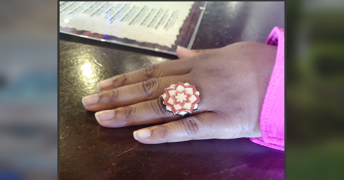 Close-up of Banvoa's hand resting on a table, showing her pink flower-shaped promise ring during the anniversary lunch